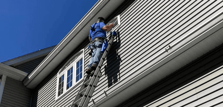 Professional window cleaning technician on ladder cleaning residential home exterior